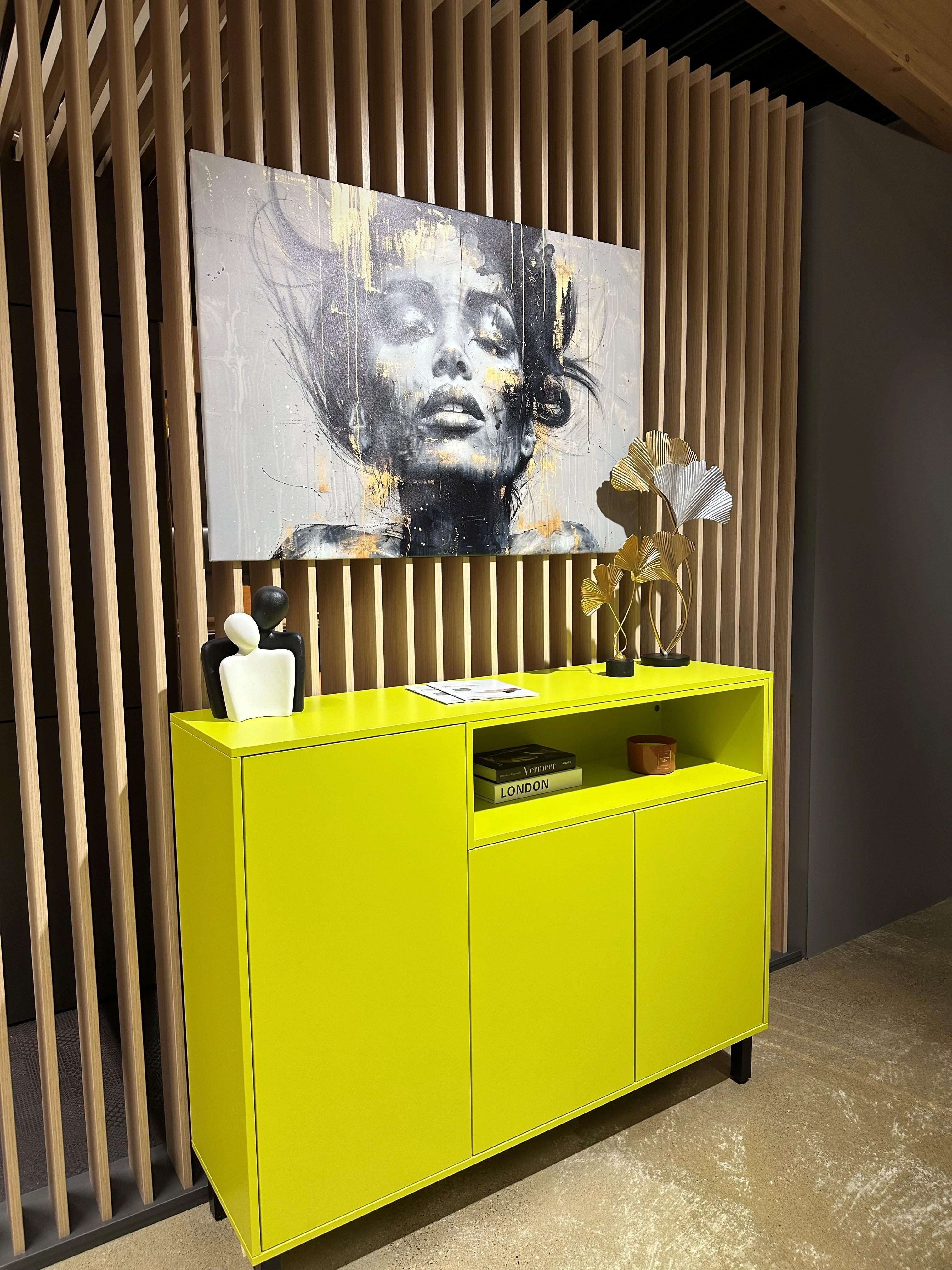 Neonfarbenes Sideboard mit einem Portrait an der Wand oben drüber.