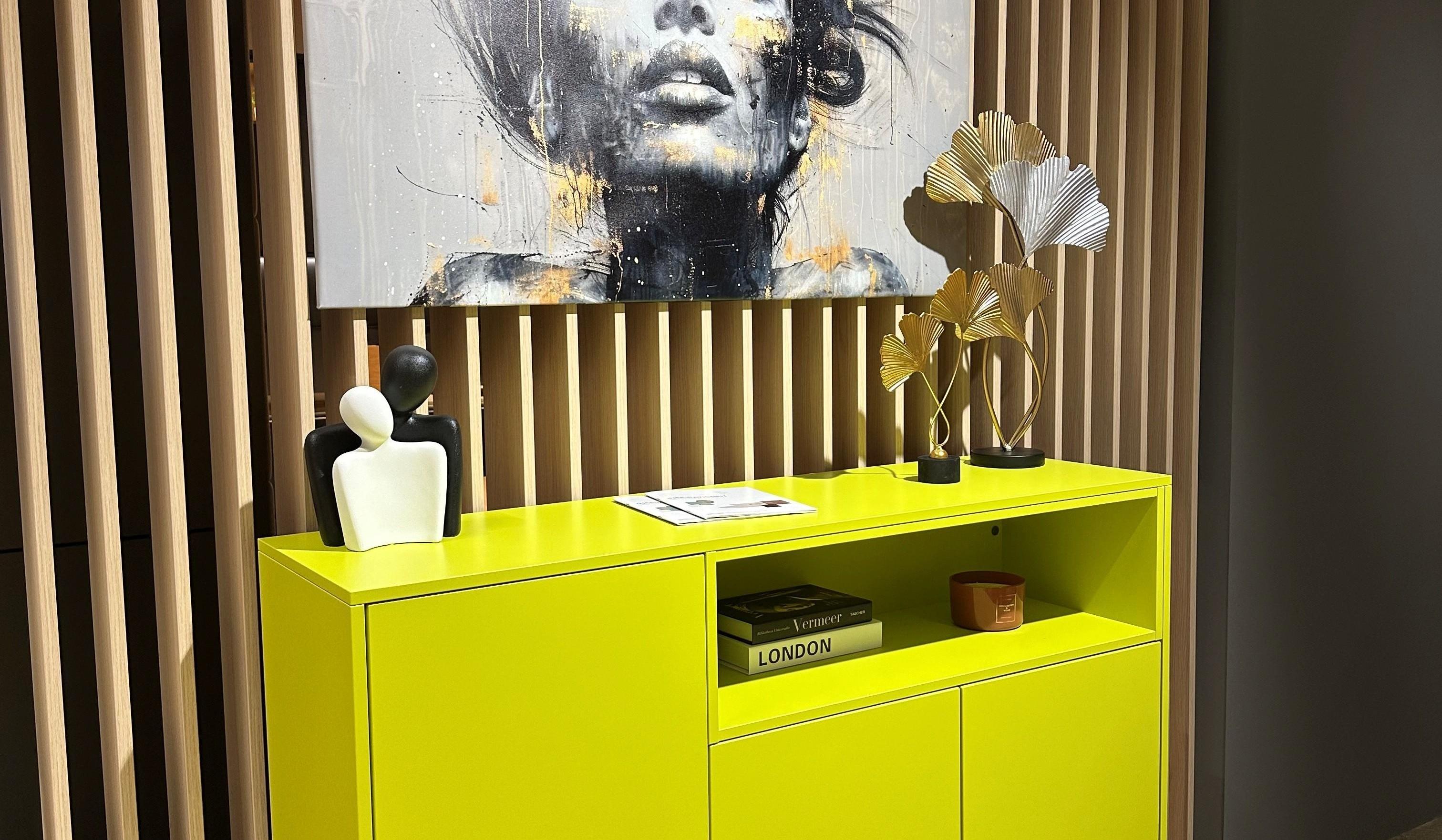 Neonfarbenes Sideboard mit einem Portrait an der Wand oben drüber.